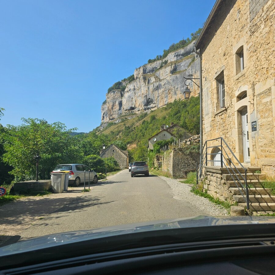 Driving past a stone building under the cliff face in the Jura