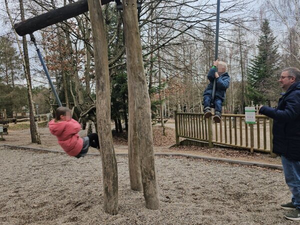 Child on a rope swing in the outdoor playground among bare trees