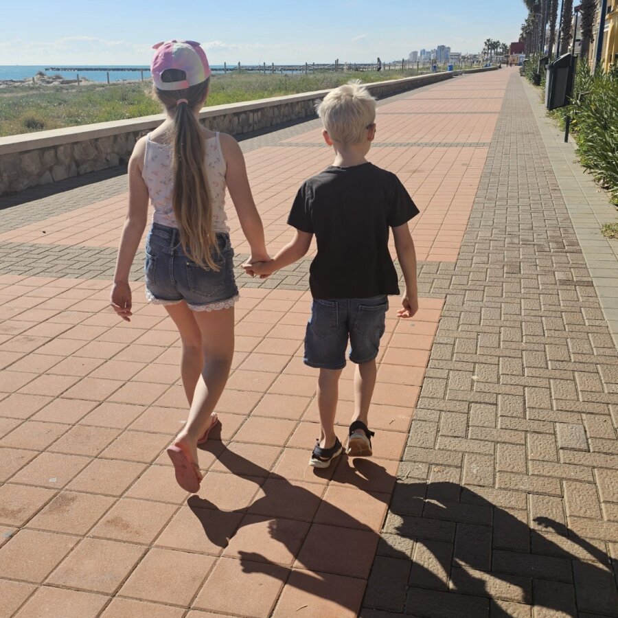 Two children walking hand in hand along the promenade in Valencia