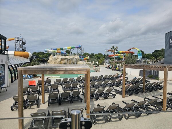 The outdoor pool complex at Camping Les Brunelles, with rows of empty sun loungers, several water slides and the covered indoor pool on the left.