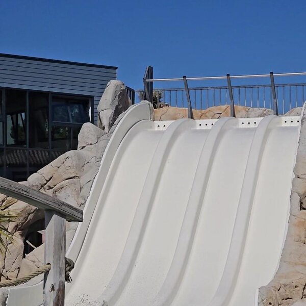 A wide white water slide with four lanes side by side against an artificial rock face at Camping Les Brunelles.
