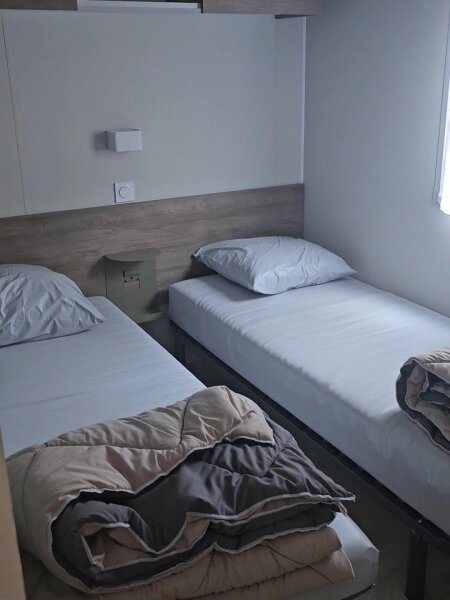 A bedroom in the Santa Fe Premium lodge with two single beds, a bedside table and overhead cupboards.