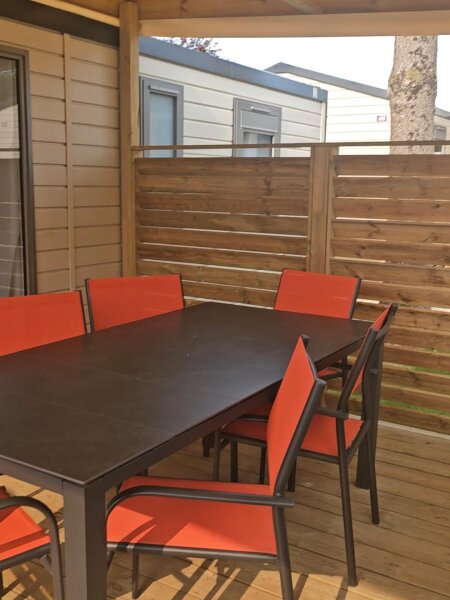 The covered wooden terrace of the Santa Fe Premium lodge with a table and six orange chairs, and the neighbouring lodge behind the fence.