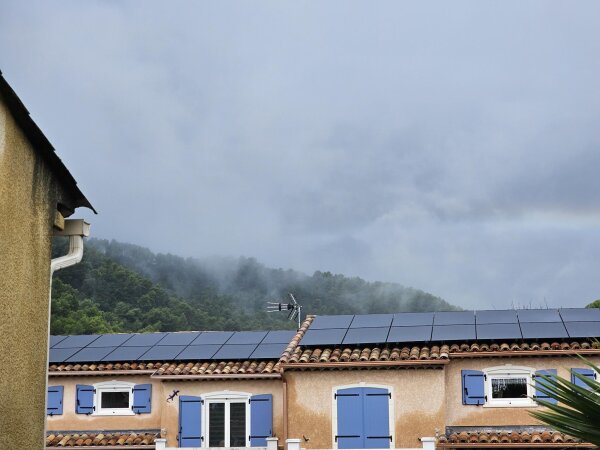 Villas with blue shutters and rooftop solar panels, with low cloud hanging over the wooded hill behind