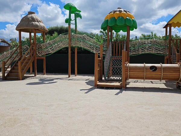 Wooden playground with climbing nets, a thatched roof and a crawl tunnel on a sandy area