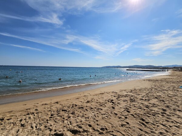 Wide sandy beach at Fréjus with swimmers in deeper water and a jetty in the distance