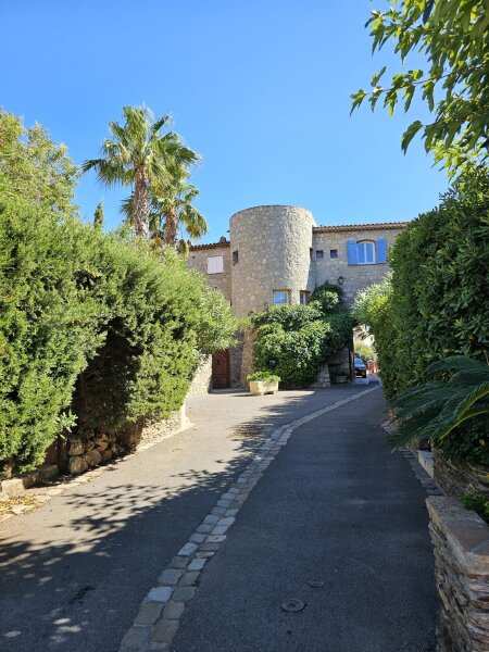 Rustige laan in Port Grimaud naar een stenen poort met ronde toren, met hoge hagen langs de weg