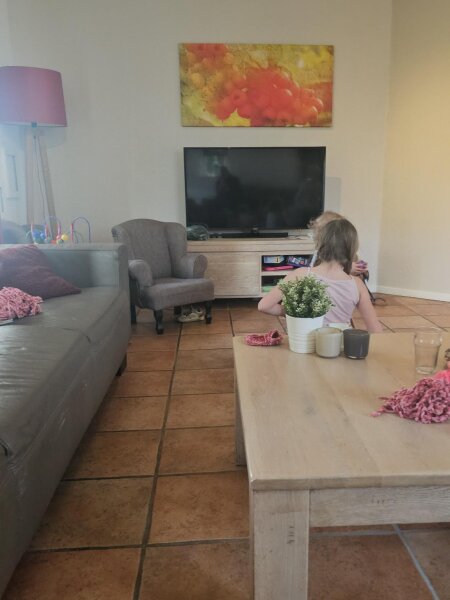 Woonkamer van het vakantiehuis met een lange bank, een fauteuil, een grote houten tafel en een tegelvloer