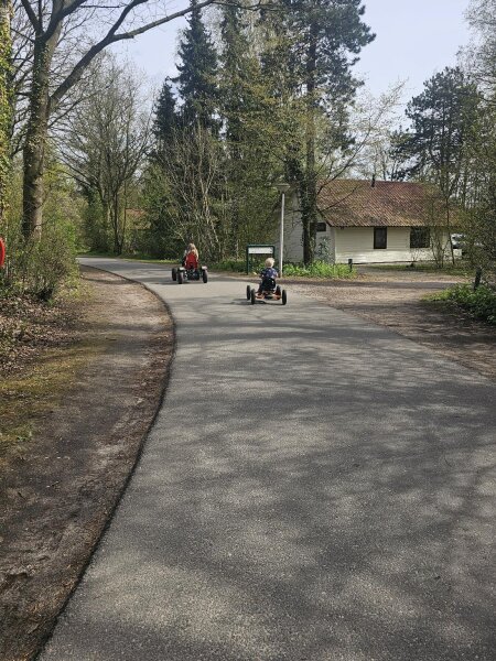 Twee kinderen op gehuurde skelters op een brede weg tussen de huisjes op het vakantiepark