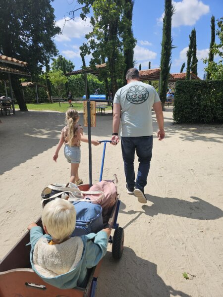 Wooden handcart loaded with bags, pulled along a sandy path past covered picnic huts
