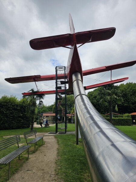 Red biplane with a metal tube slide underneath and benches alongside