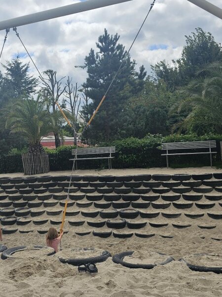 Large swing above a sand slope built from tyres, with covered benches behind it