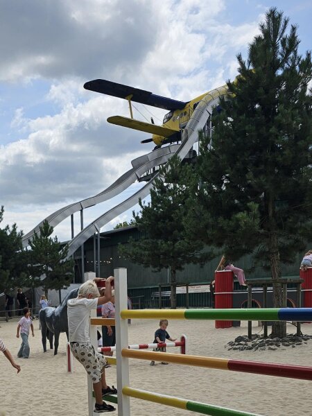 Yellow aeroplane with two long slides, with coloured jumping poles in the sand in the foreground