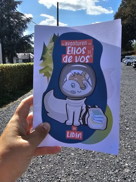 Hand holding up the booklet The Adventures of Elios the Fox in Libin in a car park