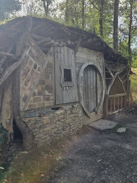 Wooden hut with a round door and a grassy roof beside a path at Domaine de Chevetogne