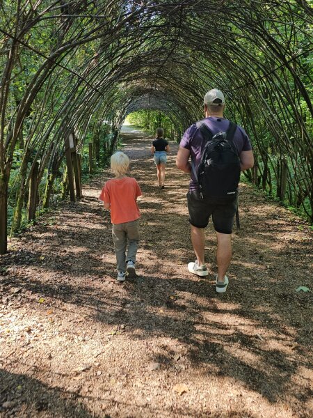Man and two children seen from behind in a long tunnel of woven willow branches